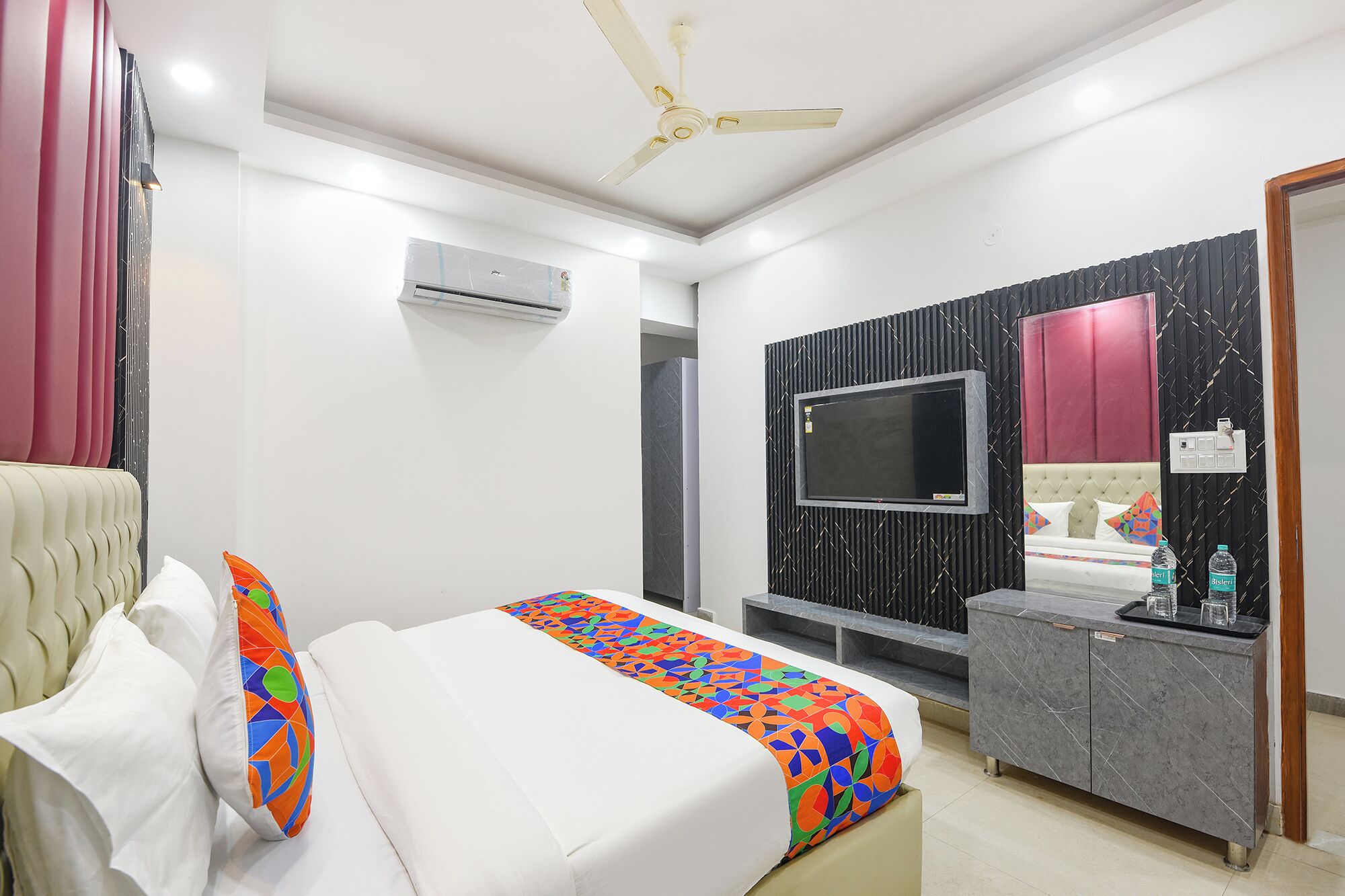 A bedroom with a bed, a TV, a vanity, and a ceiling fan.