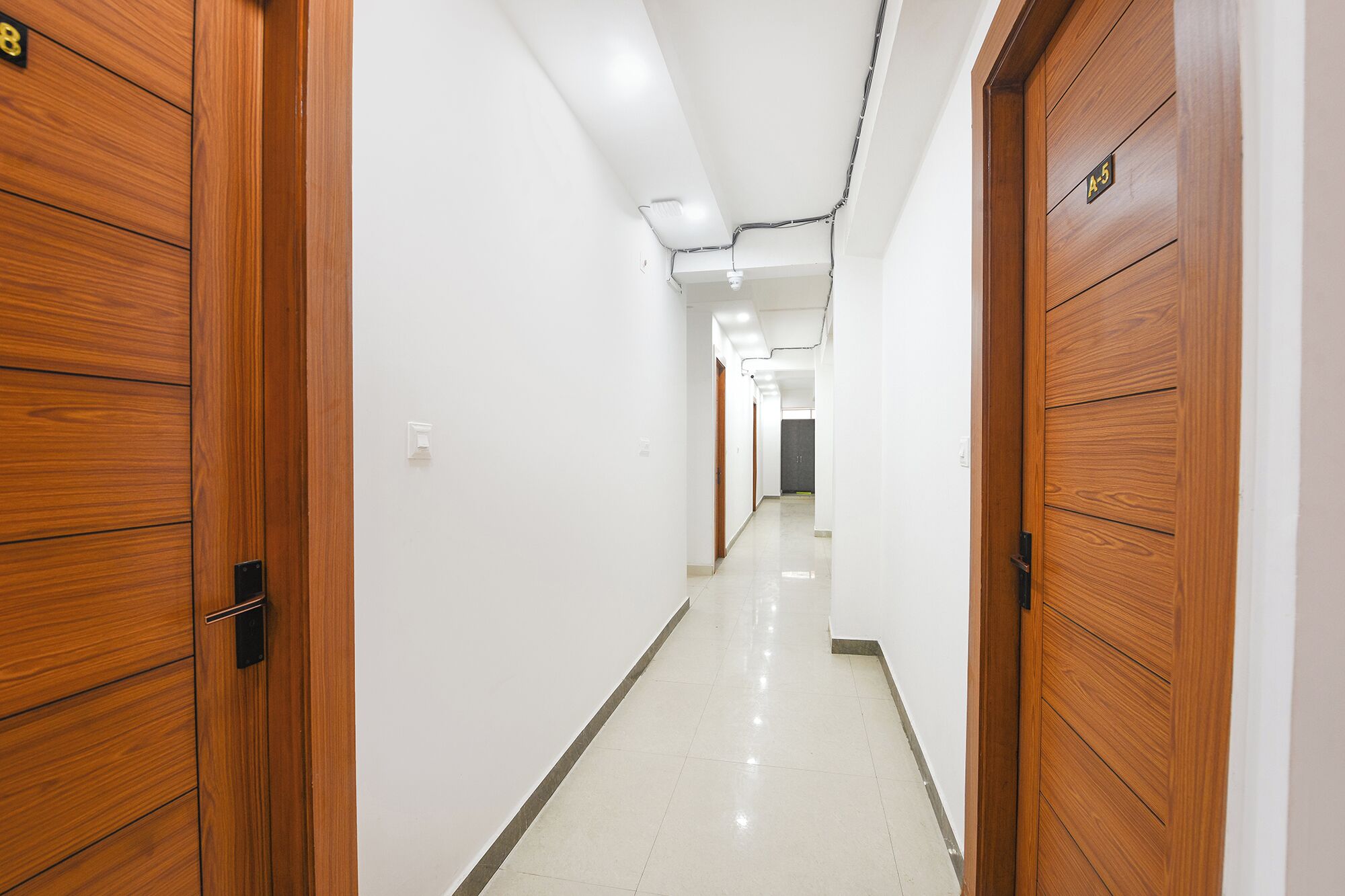 A hallway with wooden doors, white walls, and a tiled floor.