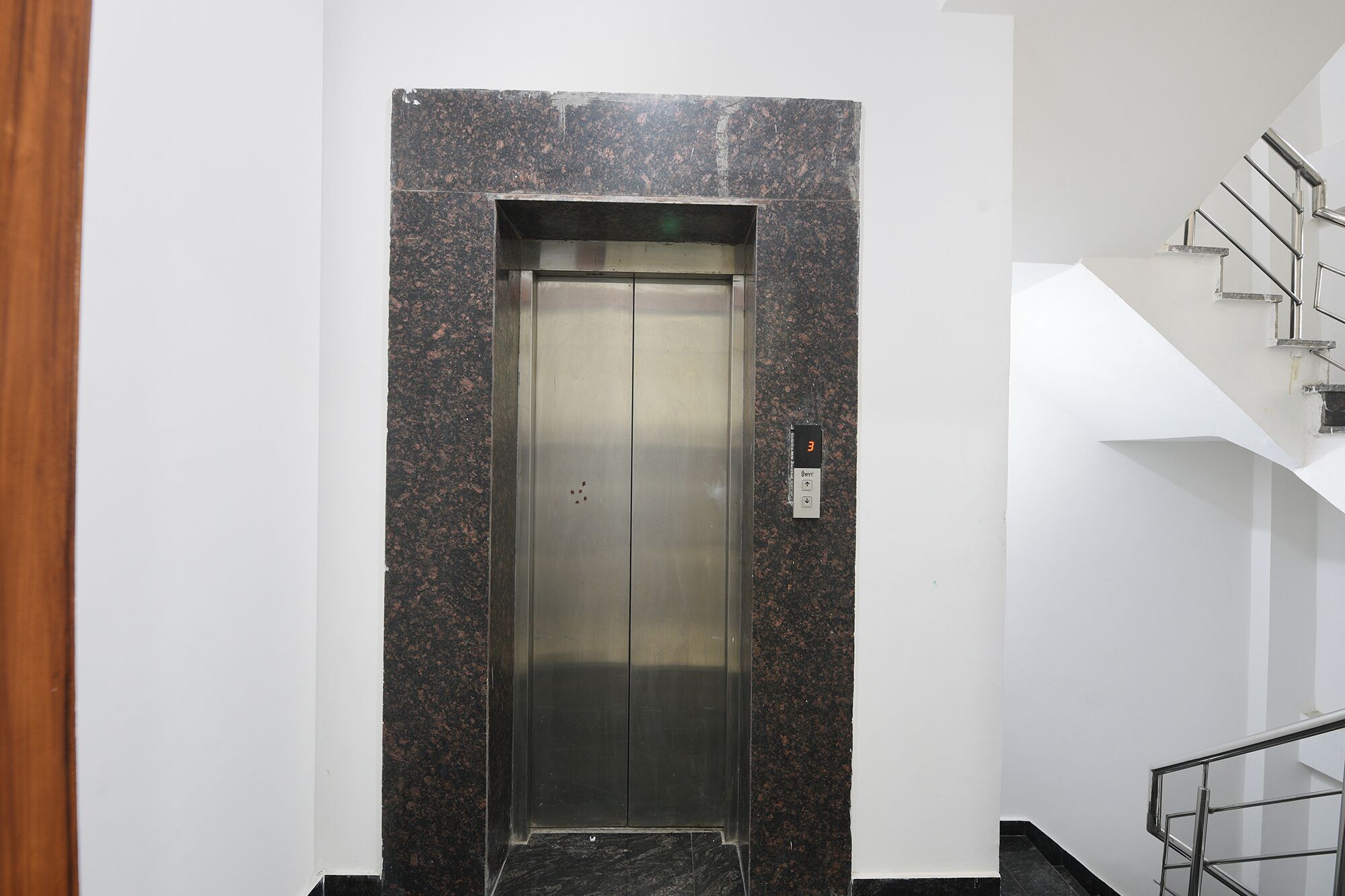 Un ascenseur moderne doté d’un écran numérique, d’un mur en granit et d’un escalier en métal.