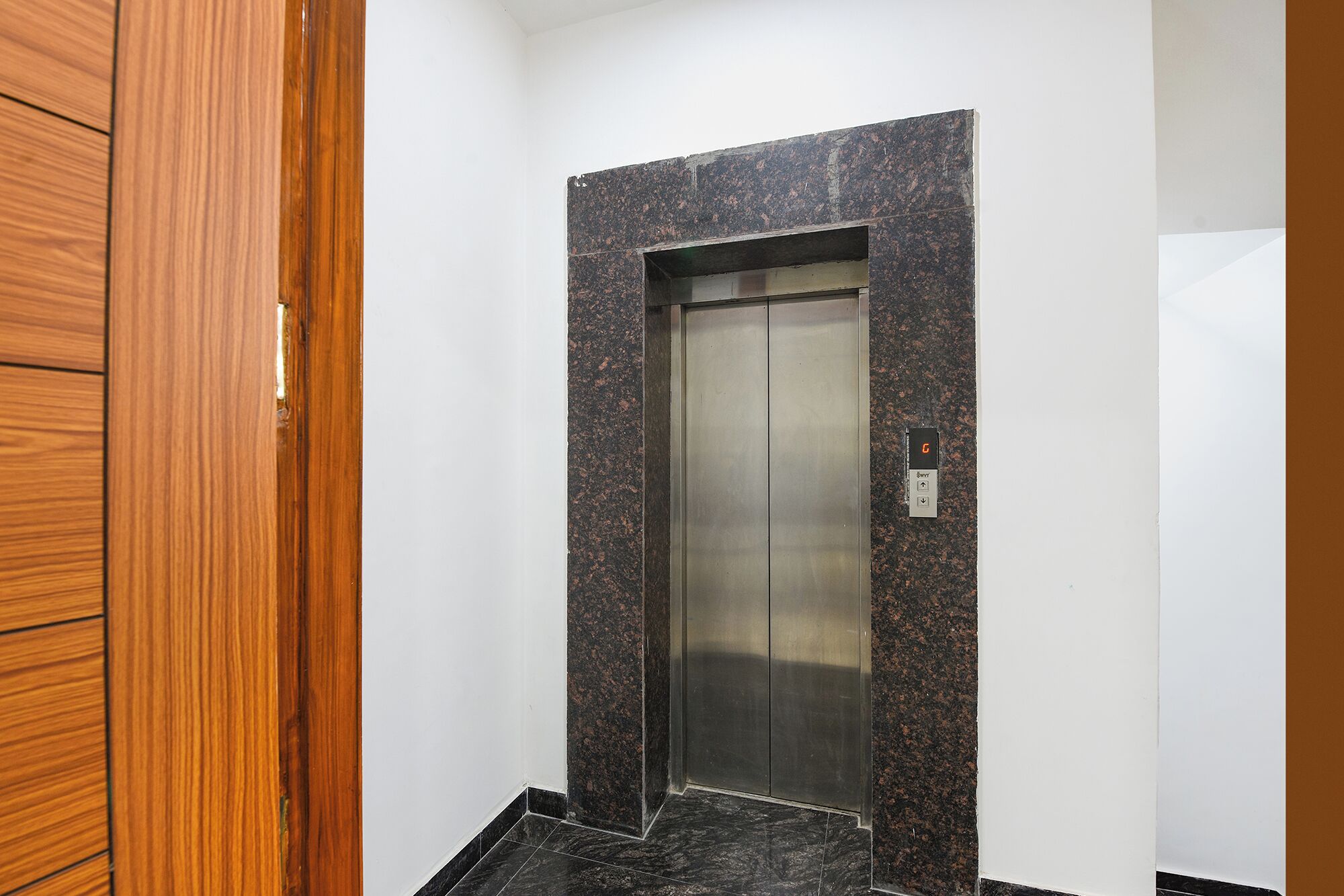 An elevator with a metallic interior, a control panel with a digital display, and a granite wall.