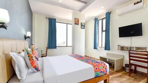 Habitación de hotel con cama, escritorio, silla y televisor en la pared.