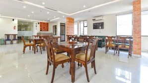 Un comedor amplio con mesas y sillas de madera, una pared de acento de ladrillo y un televisor de pantalla plana montado en la pared.