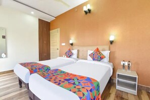 Habitación de hotel con dos camas, un armario de madera, una mesita de noche con una botella de agua y una lámpara fijada a la pared.