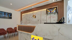 A hotel reception area with a marble counter, a large framed artwork, and a Buddha statue. - Fabhotel Global Stay (Bangalore)