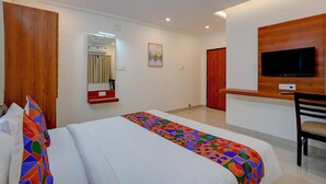 A hotel room with a bed, a desk, a chair, a television, a mirror, and a door. - Fabhotel Global Stay (Bangalore)