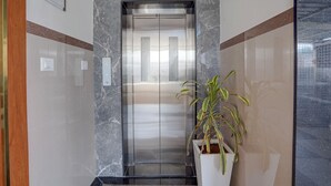 An elevator with a marble wall and a potted plant beside it. - Fabhotel Global Stay (Bangalore)