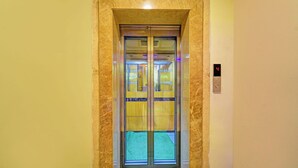 Ascensore con display digitale che mostra il numero 4, porta in vetro e tappeto verde sul pavimento.