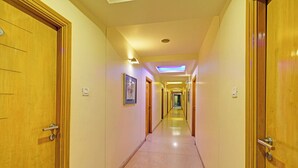 Corridoio di un hotel con porte in legno, pavimento piastrellato e illuminazione a incasso.