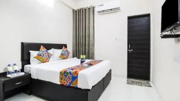 Habitación de hotel con una cama negra, paredes blancas y una puerta negra.