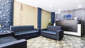 Zona de recepción con pared de diseño de piedra, mostrador de recepción y dos sofás oscuros.