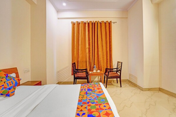 A hotel room with a bed, a small table with two chairs, a window with curtains, and a colorful bedspread. - FabHotel HM Residency (Noida)