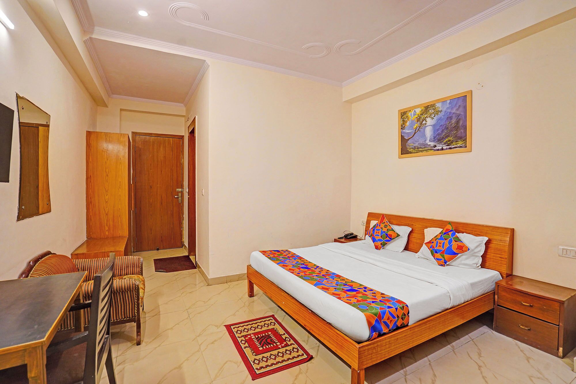 A bedroom with a bed, bedside table, nightstand, wooden chair, dining table, and a rug.