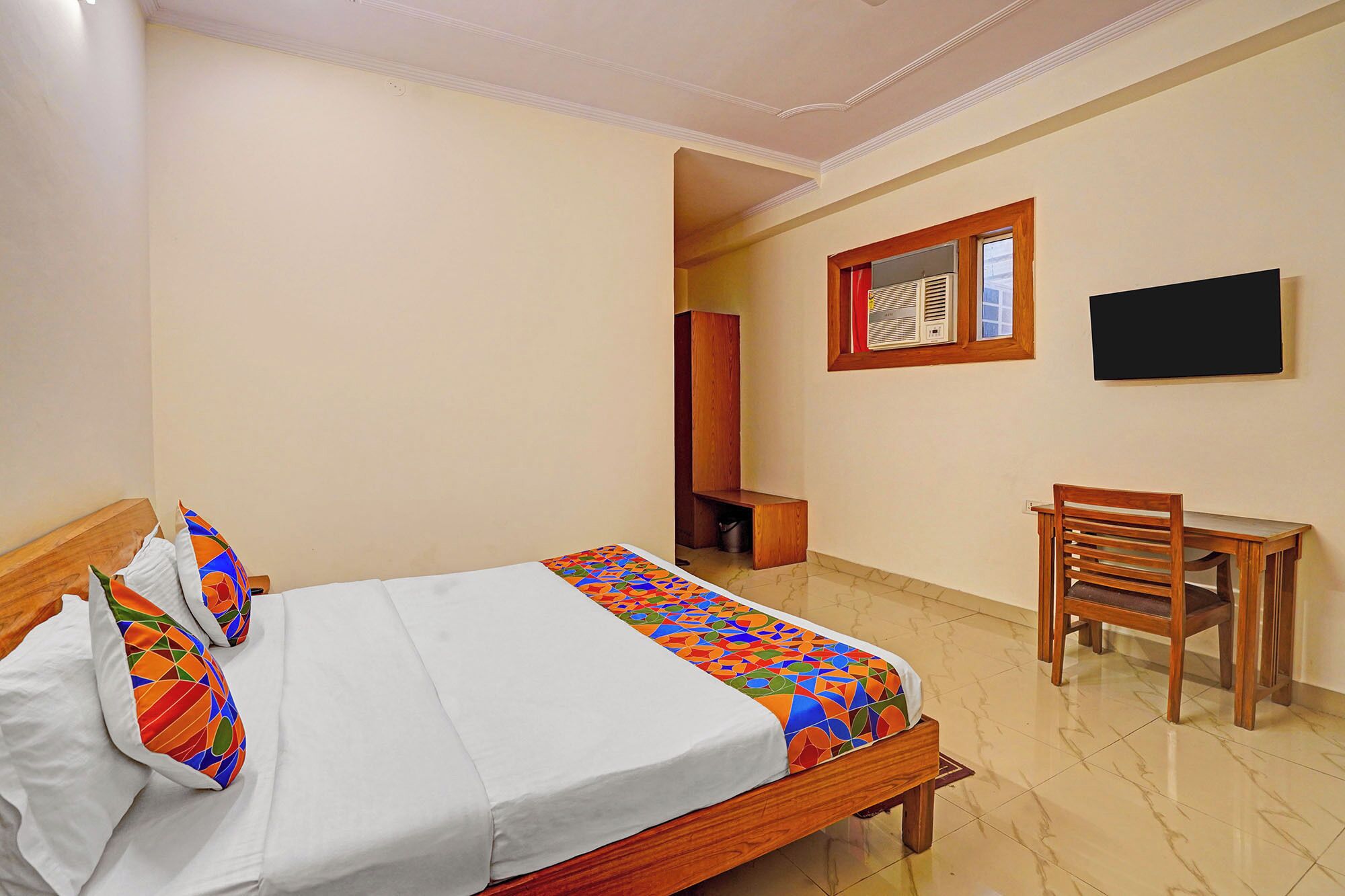 A hotel room with a bed, a desk, a chair, a television, and a mirror.