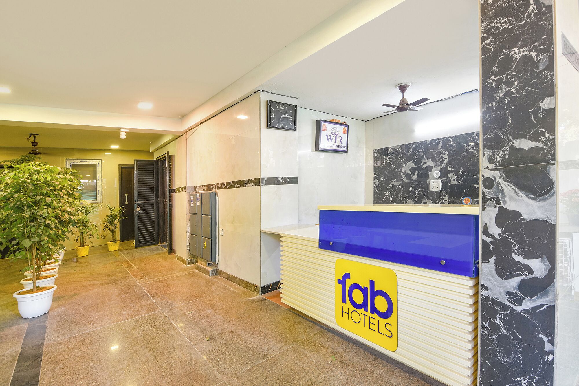 A hotel reception desk with a sign reading 'fab hotels,' a clock, and a marble wall.