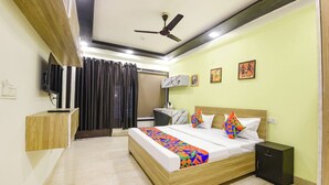 Ein Hotelzimmer mit Bett, Nachttisch, Kleiderschrank, Deckenventilator und Kunstwerken an den Wänden.