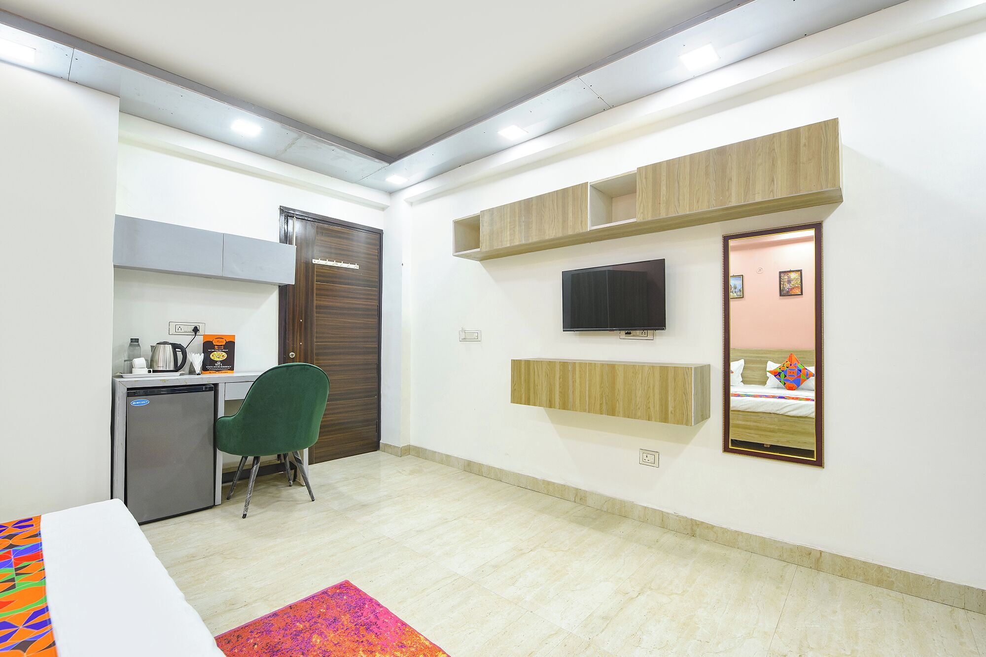 Habitación de hotel con escritorio, silla, televisión, espejo y cama con almohadas.