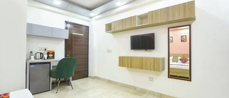 Habitación de hotel con escritorio, silla, televisión, espejo y cama con almohadas.
