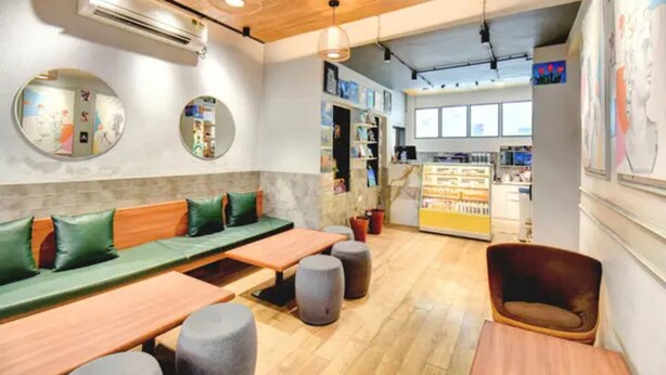 Un café con mesas de madera, bancos acolchados de color verde y una barra con diversos artículos.