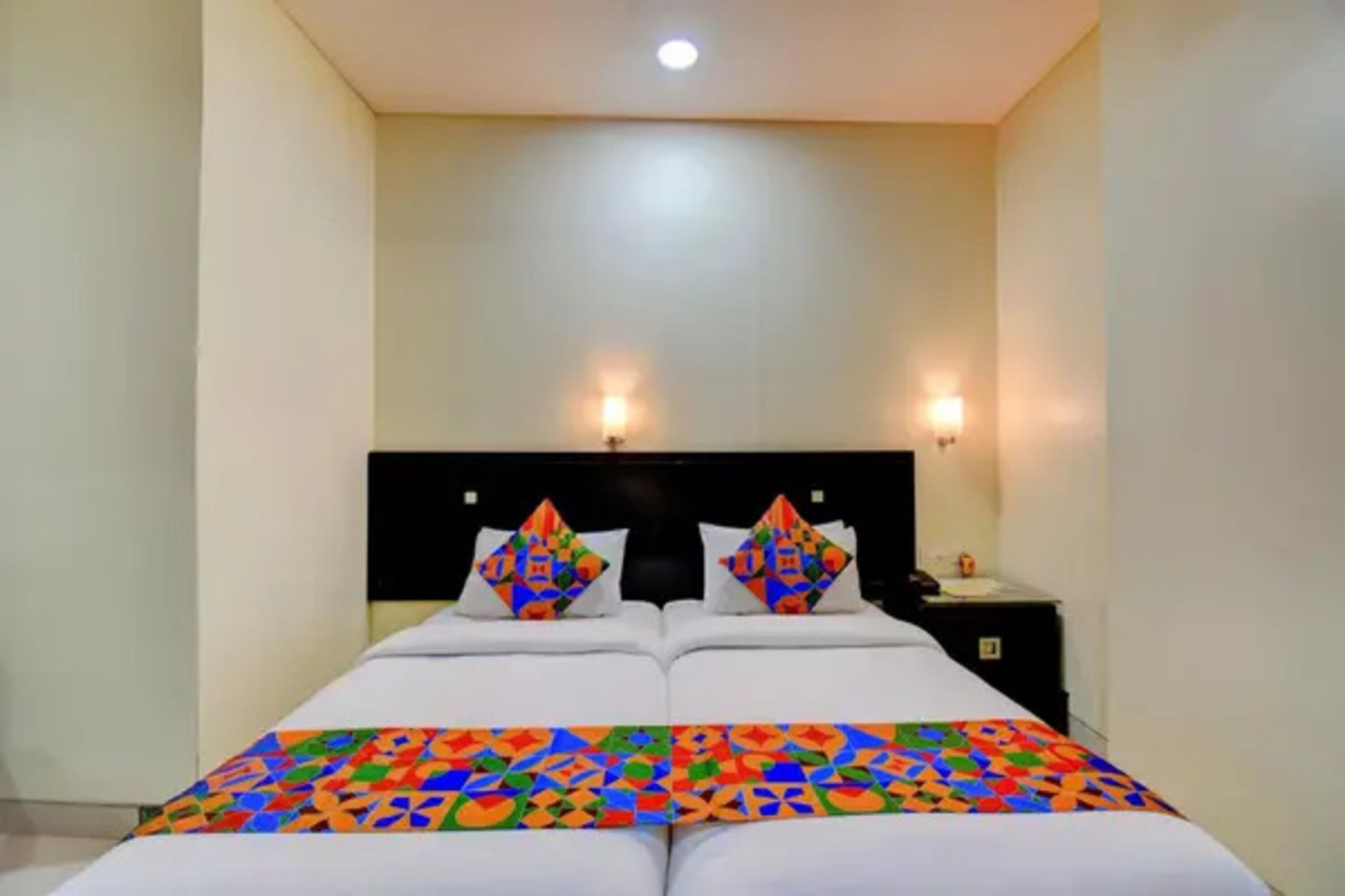 Un letto matrimoniale con una coperta colorata a motivi geometrici, due cuscini coordinati, una testiera nera e due luci a parete.