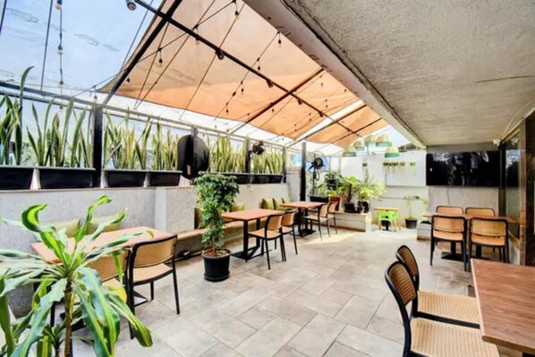 An outdoor patio area with tables and chairs, potted plants, and a glass ceiling structure.