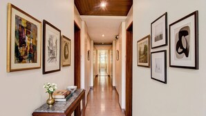 Un pasillo con obras enmarcadas en las paredes, una mesa de mármol con un florero y libros, y un techo de madera.