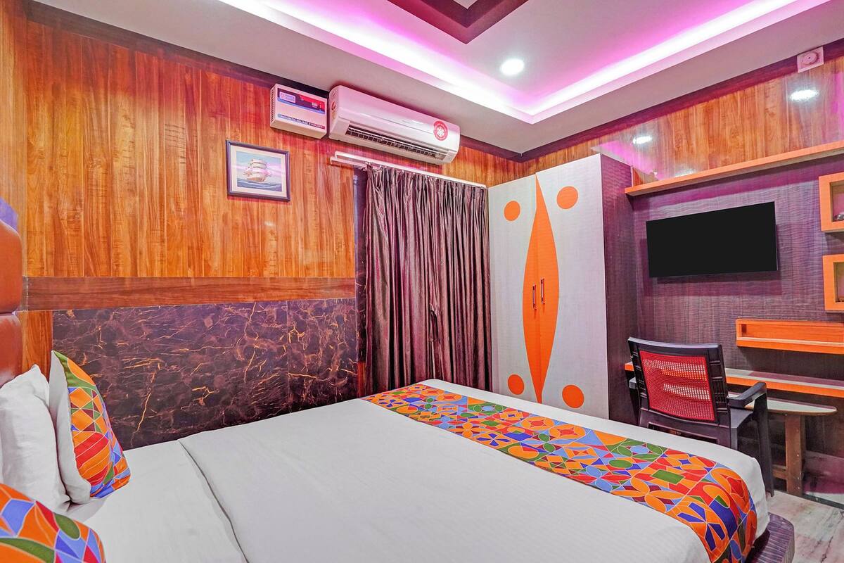 A hotel room with a bed, a desk, a TV, and an air conditioning unit.
