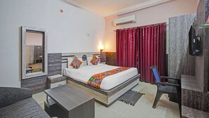 Une chambre d’hôtel équipée d’un lit, d’un bureau, d’une chaise, d’un ventilateur de plafond, d’un climatiseur, d’un miroir et d’un rideau rouge.