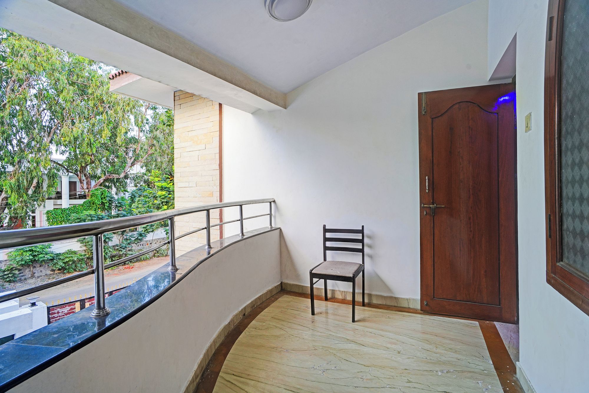 Un balcón con una silla, una puerta de madera y vistas al verdor.