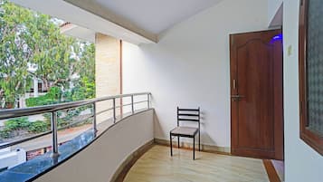 A balcony with a chair, a wooden door, and a view of greenery.
