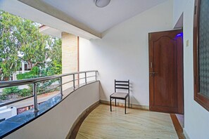 Ein Balkon mit einem Stuhl, einer Holztür und Blick ins Grüne.