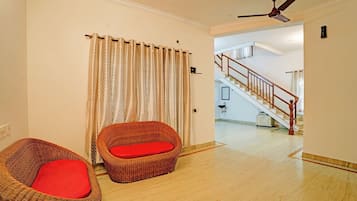A room with a wicker chair with a red cushion, a curtain, a ceiling fan, and a staircase leading to another level.