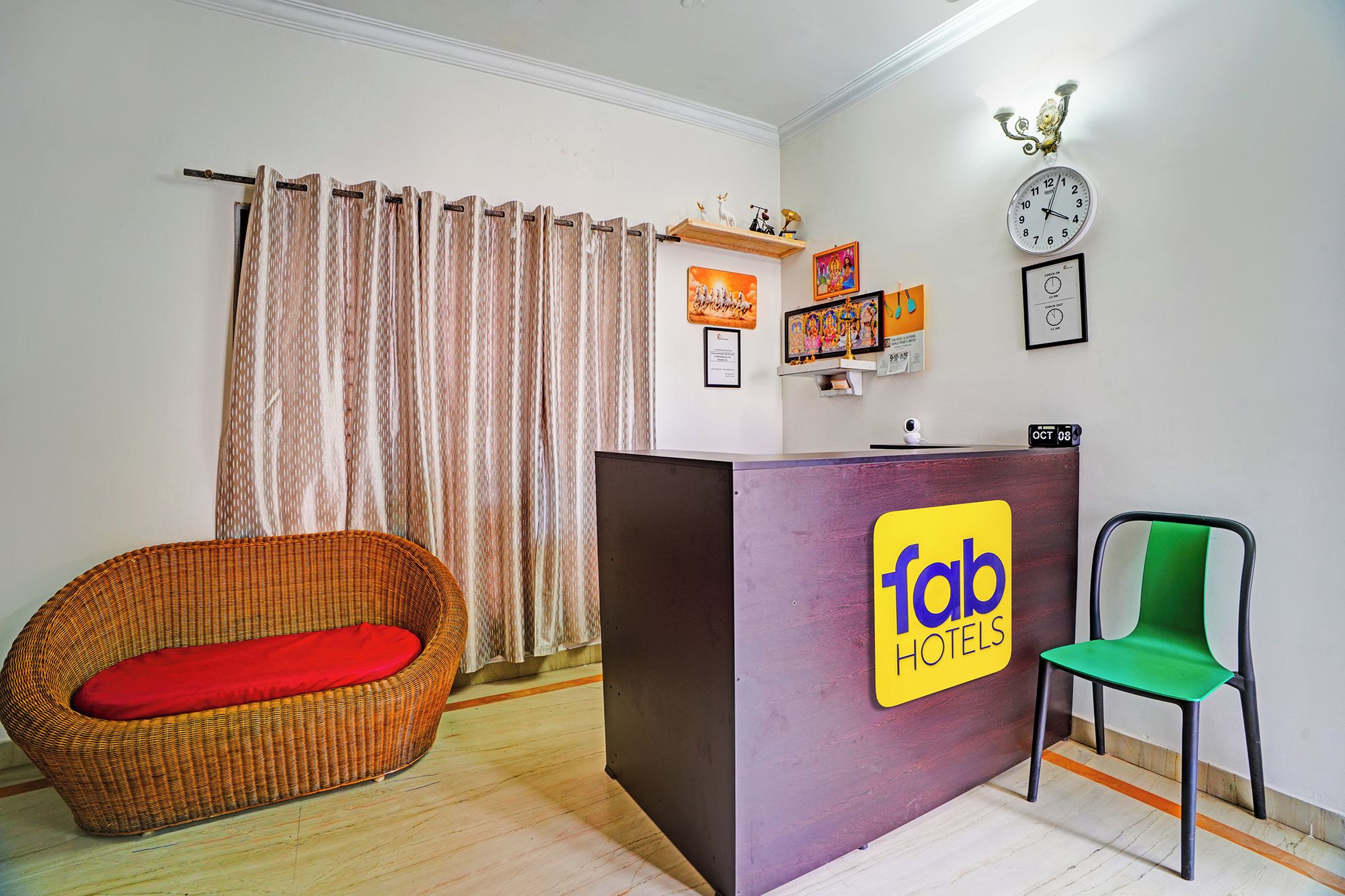 Una recepción con un cartel de 'Tab Hotels', una silla de mimbre con cojín rojo, una silla verde y un reloj en la pared.