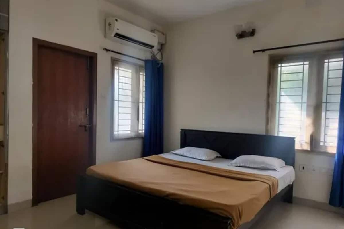 Une chambre à coucher avec un lit, une fenêtre avec des rideaux, un appareil de climatisation et une porte.