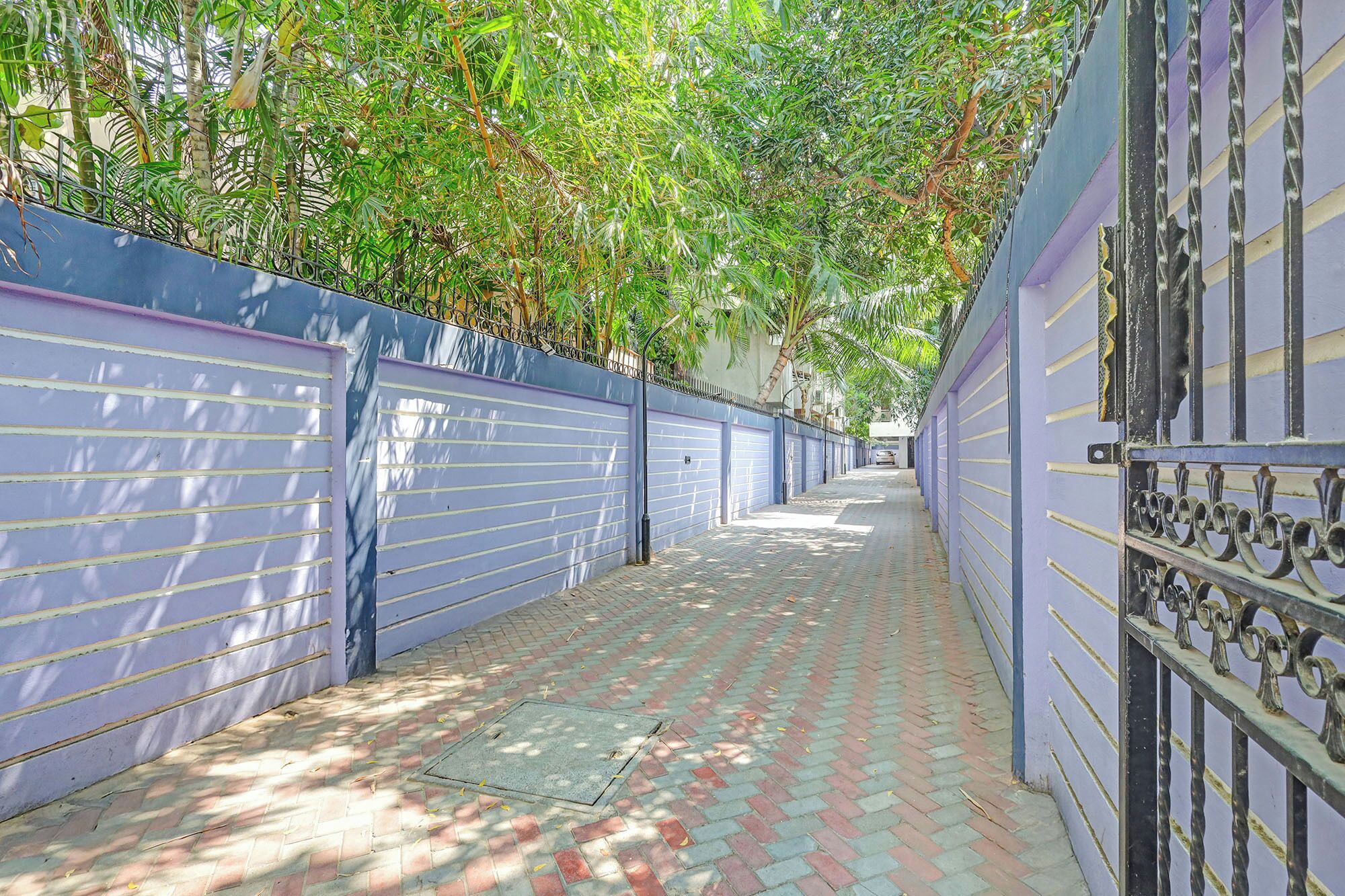 A narrow alleyway with a blue wall, a metal gate, and a brick-paved path.