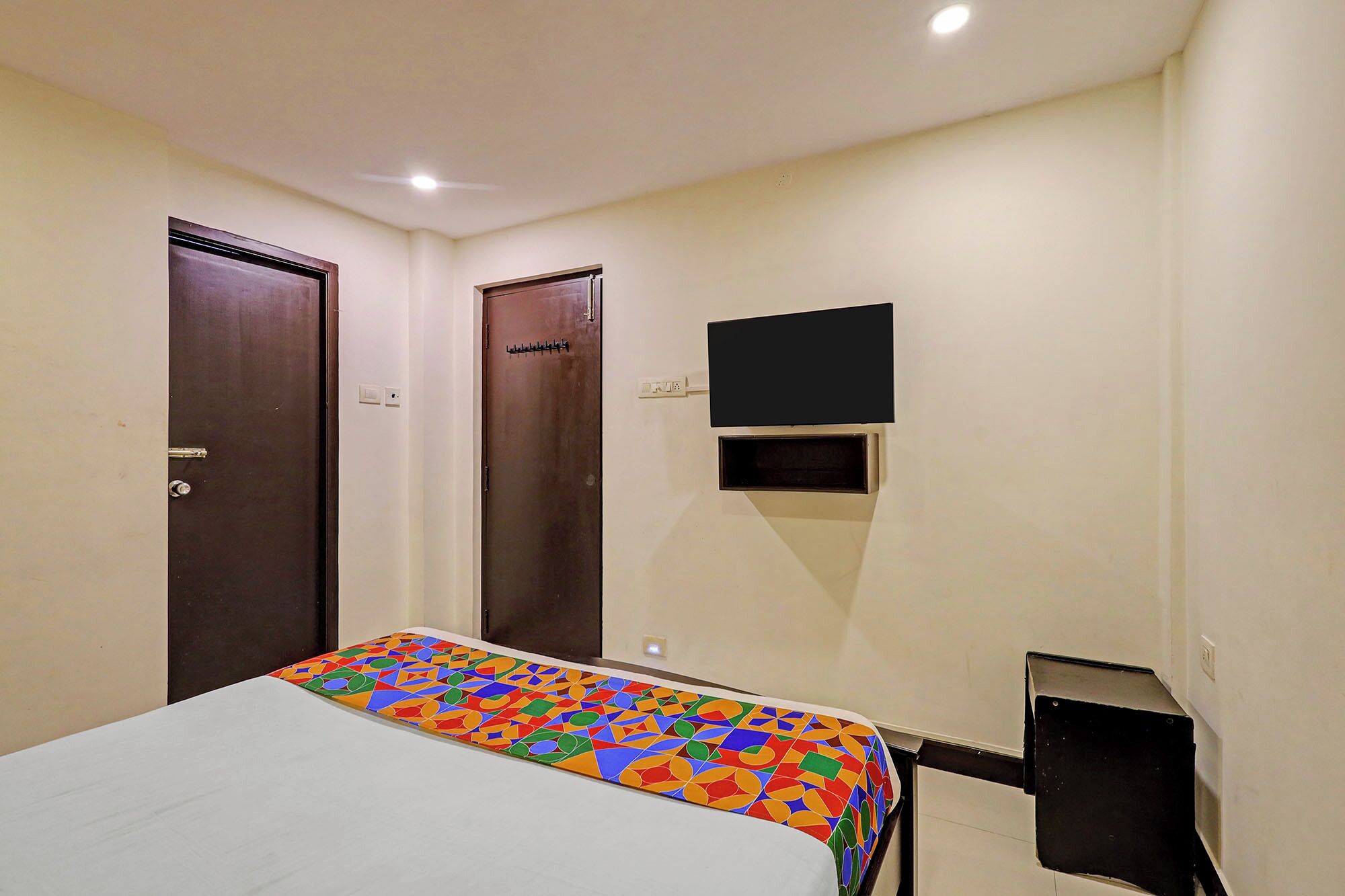 A hotel room with a bed, a TV mounted on the wall, and two doors.
