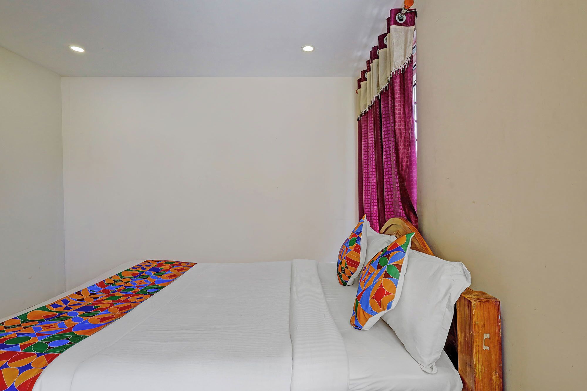 A single bed with a white sheet, a colorful bedspread, and a wooden headboard.