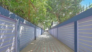 A corridor with a tiled floor, flanked by blue walls with horizontal lines, leading to a building entrance. - Fabhotel Neha (Chennai)