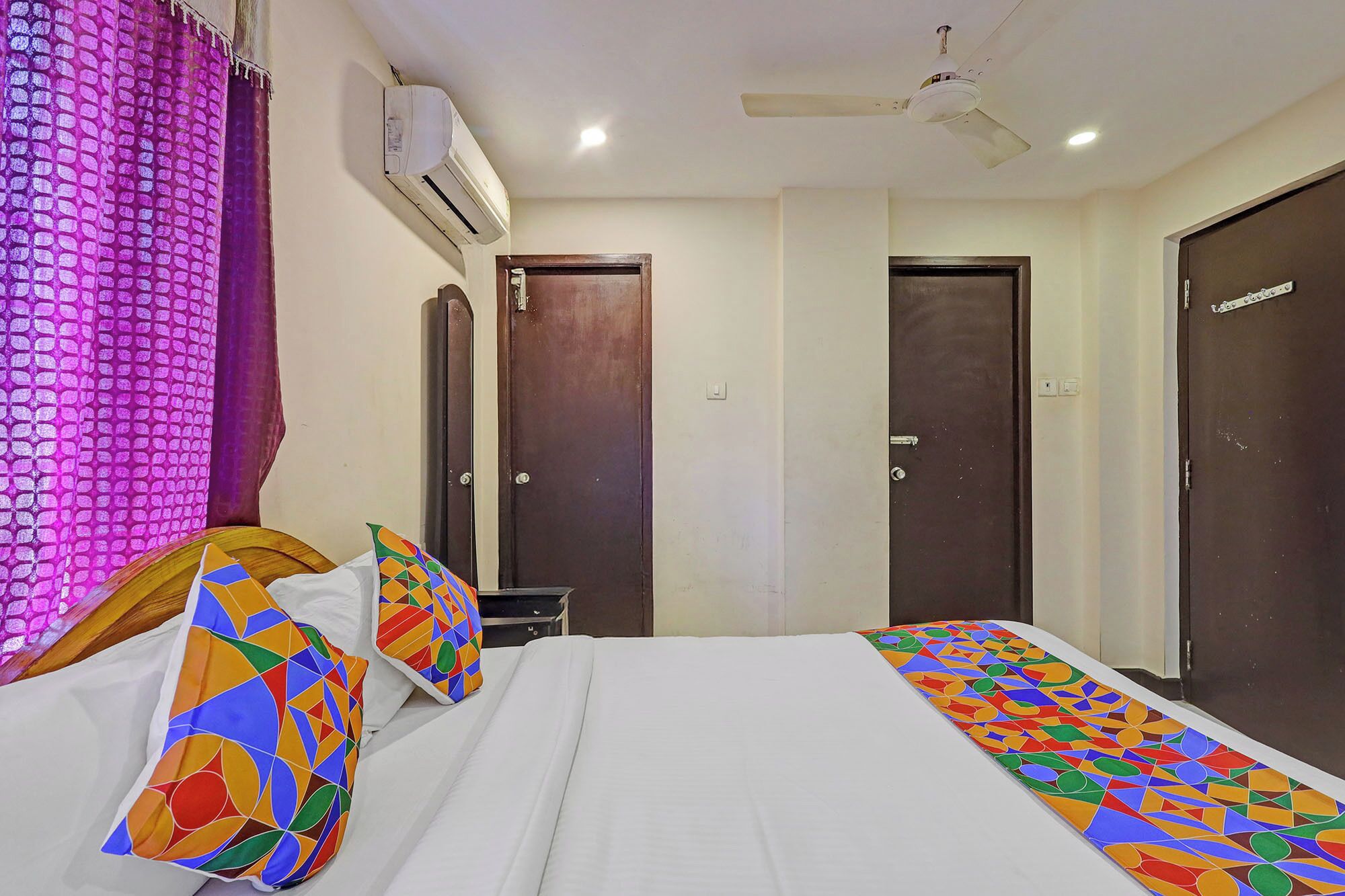 A hotel room with a bed, a ceiling fan, an air conditioning unit, and two doors.