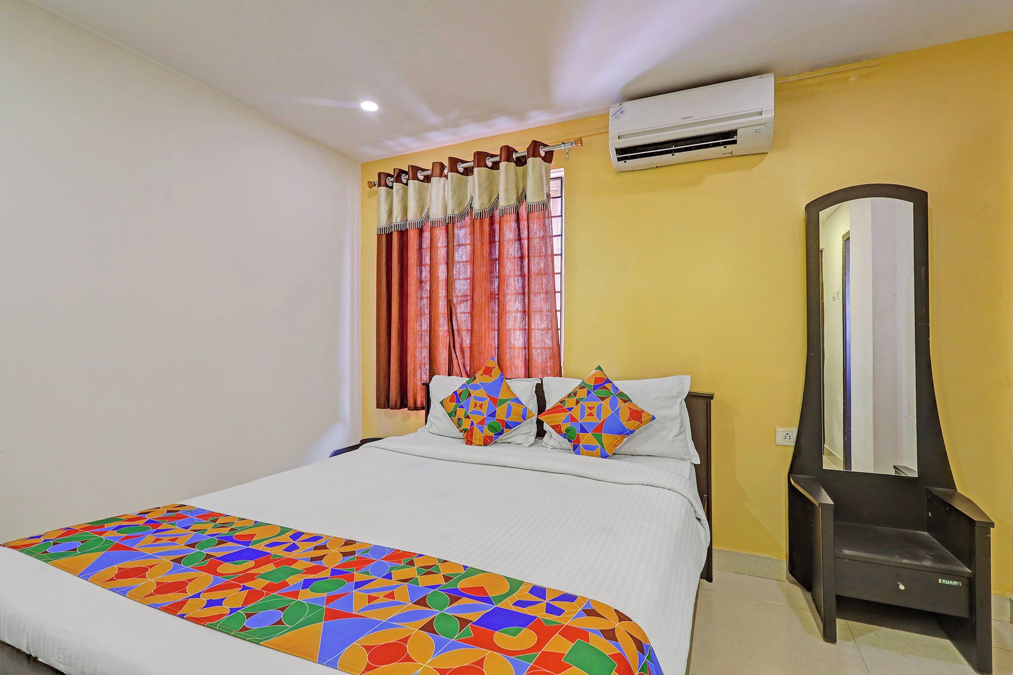 A hotel room with a bed, a mirror, an air conditioning unit, and curtains.