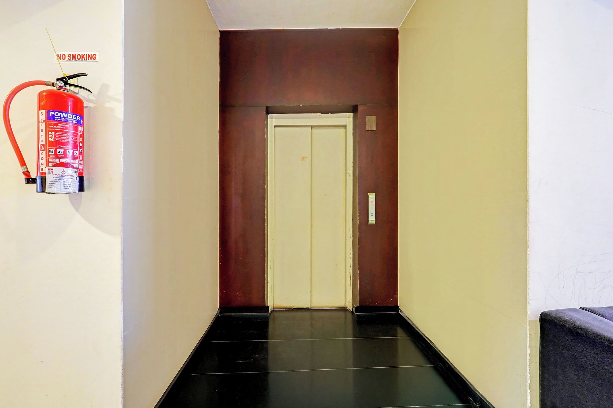 A hallway with a fire extinguisher mounted on the wall, a closed door at the end, and a small sign indicating a smoking zone.