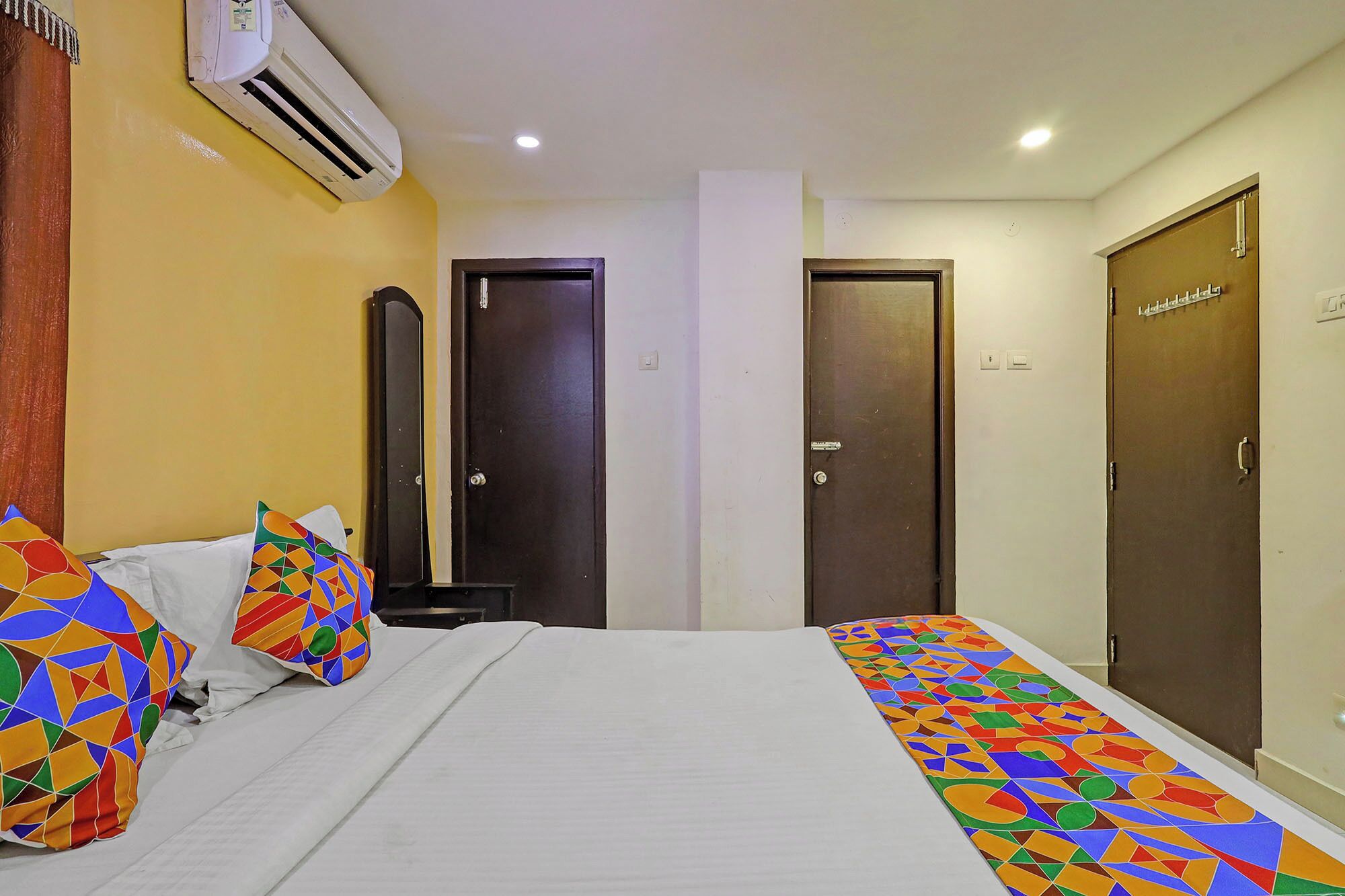 A hotel room with a bed, two doors, an air conditioning unit, and a patterned bed runner.