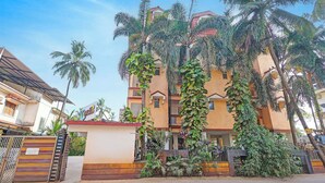 Un edificio de varios pisos con entrada protegida por una reja, rodeado de abundante vegetación y palmeras.