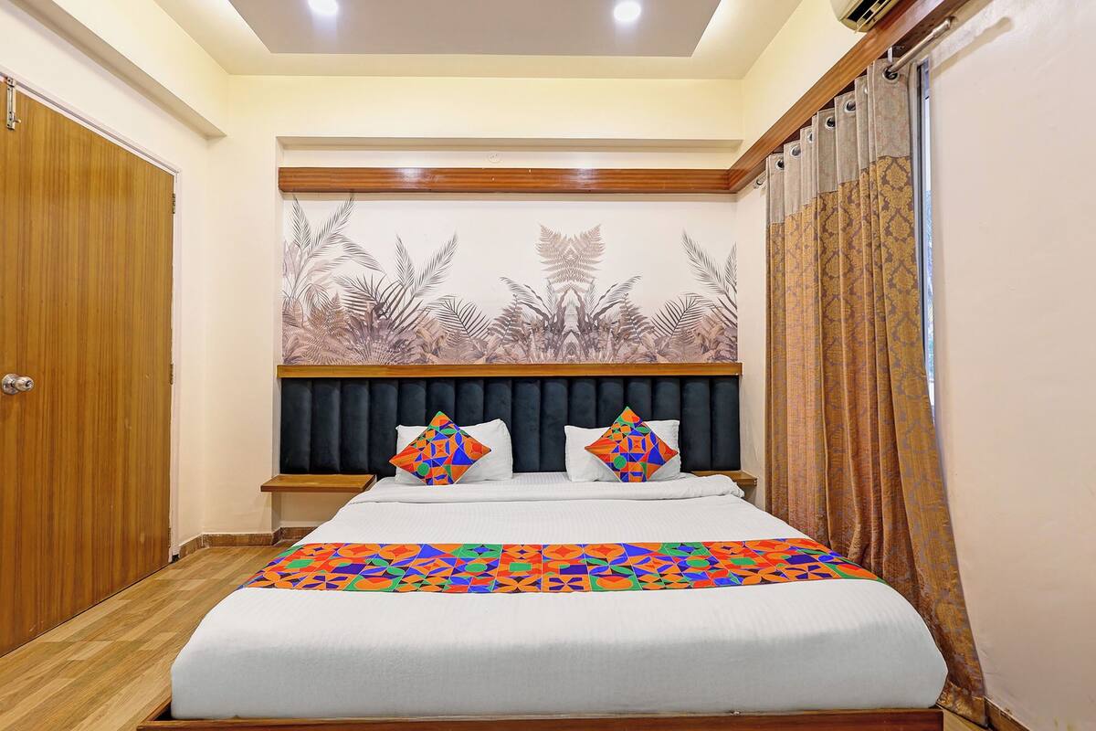 Quarto com cama, cabeceira, painel na parede e janela com cortinas.