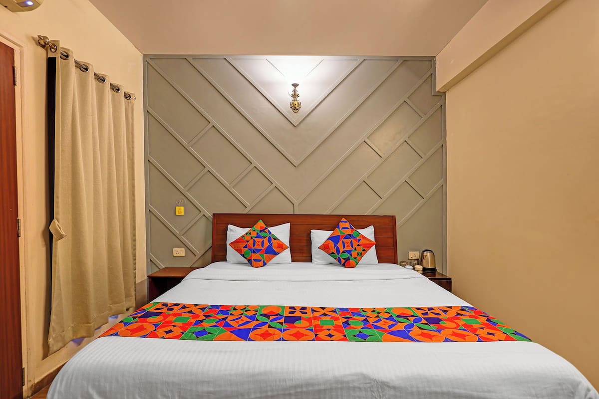 Quarto de hotel com cama, mesa de cabeceira, abajur e janela com cortinas.
