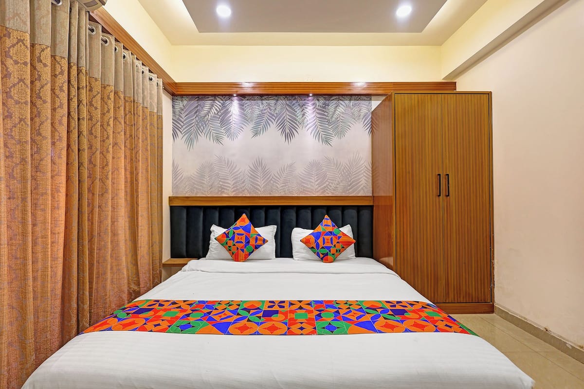 Quarto com cama, duas almofadas, cabeceira, guarda-roupa e cortinas.