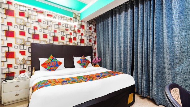 Quarto de hotel com cama, mesa de cabeceira, uma cadeira e parede estampada.