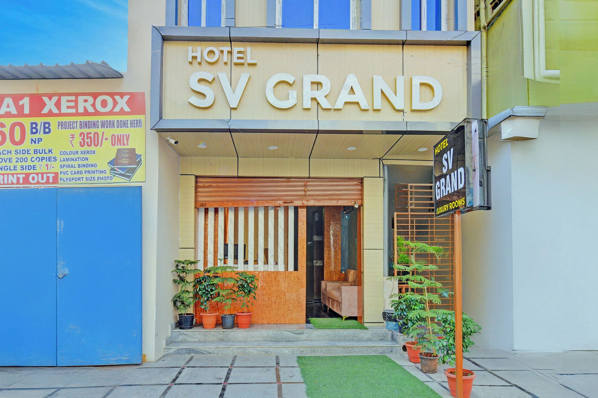 A hotel entrance with a sign reading 'HOTEL SV GRAND' and a sign for 'XEROX' advertising printing services.