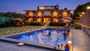 A hotel with a swimming pool, outdoor seating, and a well-lit entrance. - Fabhotel Green Crystal (Mahabaleshwar)