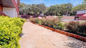 A paved pathway leading to a building with a red roof, surrounded by greenery and trees. - Fabhotel Green Crystal (Mahabaleshwar)