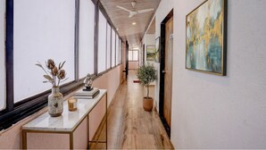 A hallway with a ceiling fan, large windows, a potted plant, and a painting on the wall. - Fabhotel Green Crystal (Mahabaleshwar)